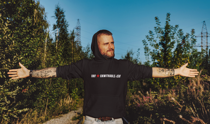 Man wearing a black hoodie with text, standing outdoors with arms outstretched.